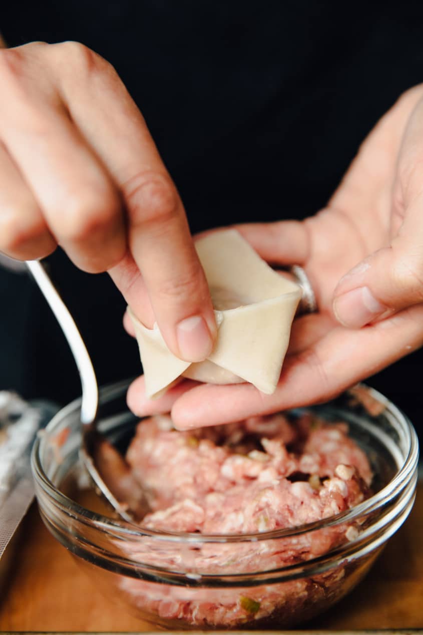 Someone is folding a wonton dumpling after a small scoop of meat is filled inside