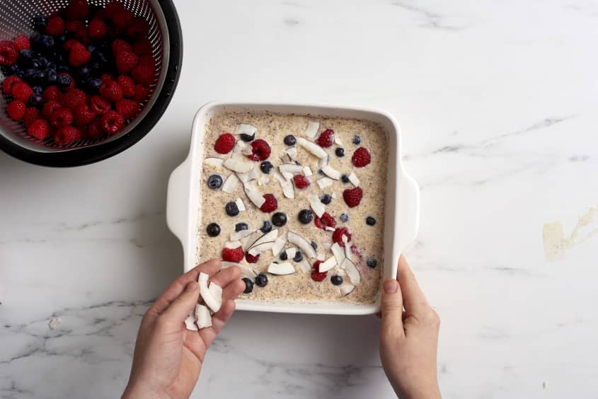 Oatmeal in a baking dish topped with fresh blueberries and raspberries, and toasted coconut