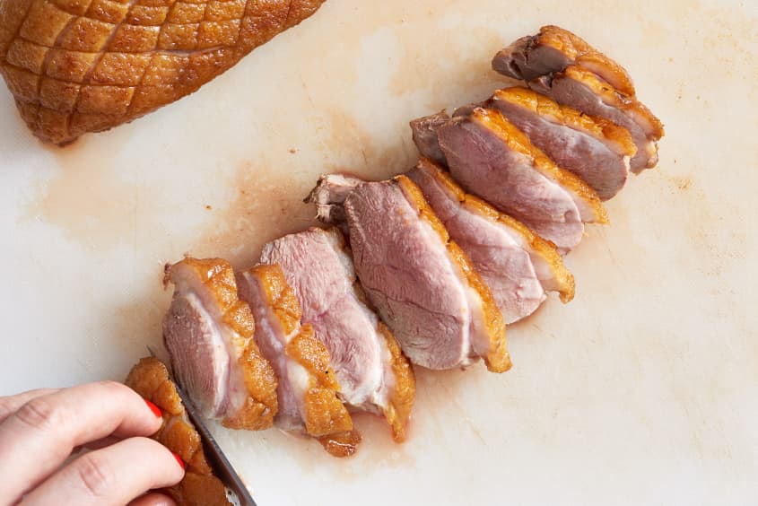 A person slicing cooked duck breast on a chopping board,  showcasing the meat's rosy interior