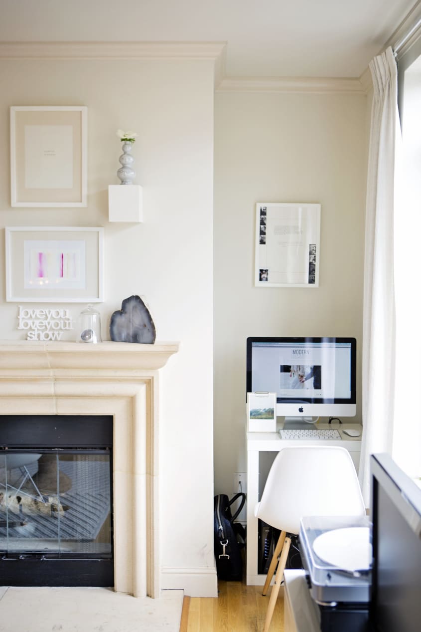a tiny white desk with computer and white chair sits in a far corner of a neutral-toned living room