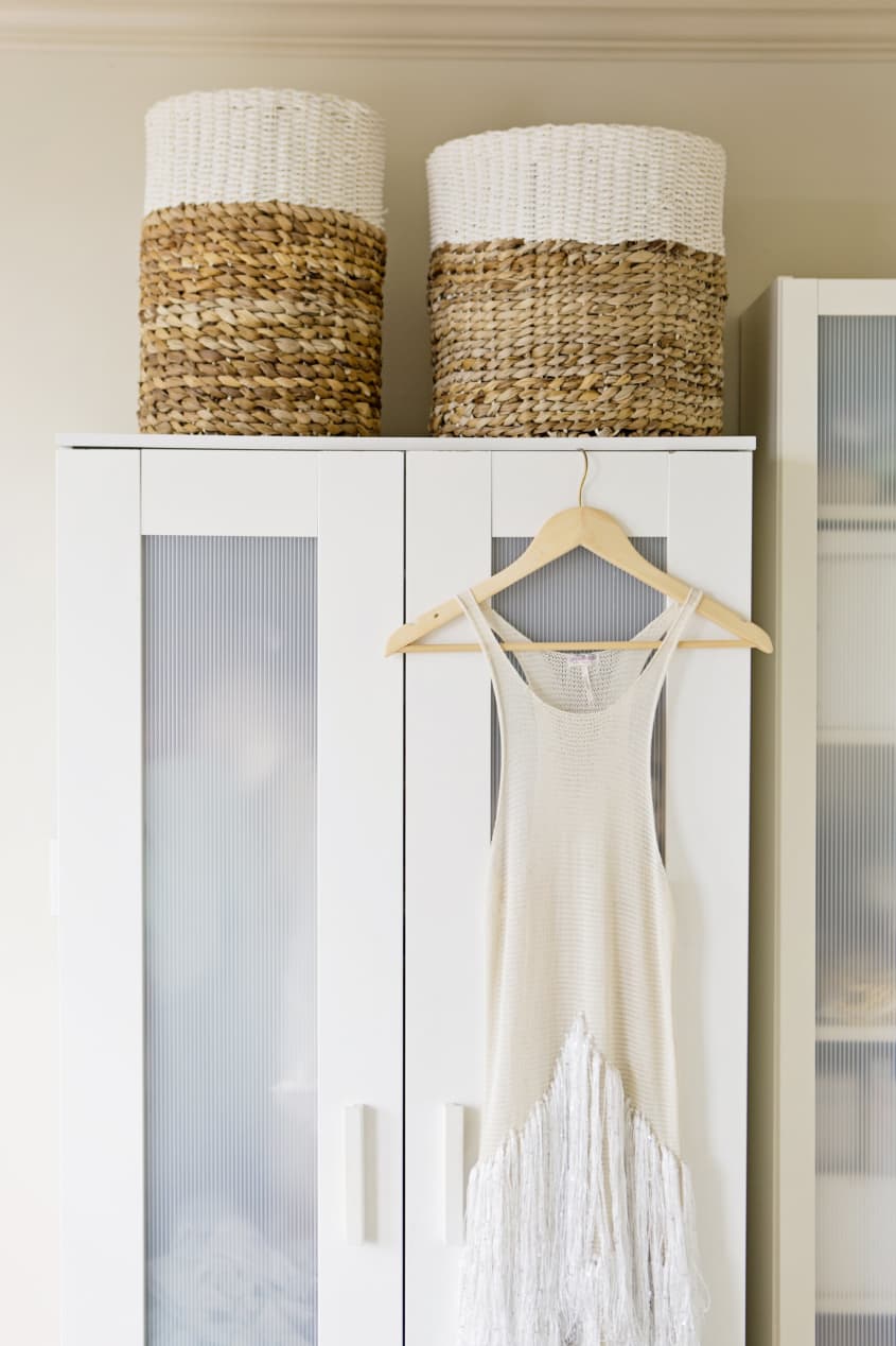 Dress hanging in front of white wardrobe with frosted glass, two storage baskets on top of the wardrobe