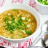 Bowl of egg drop soup garnished with chopped green onions, next to a spoon.