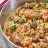Chicken breasts in creamy mushroom sauce garnished with parsley in a skillet.
