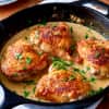 Golden-brown chicken thighs in a creamy sauce, garnished with fresh parsley in a cast-iron skillet.