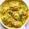 Chicken thighs in a creamy turmeric sauce with sliced onions and fresh cilantro in a skillet.