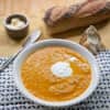 Bowl of Moroccan-spiced carrot soup with a dollop of cream, served with crusty bread and butter.
