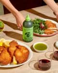 Breaded cutlets with lemon wedges, green salad, olive oil bottle, and two glasses of red wine on a wooden table.
