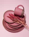 Stacked pink ceramic plates with a matching mug and dried flowers.