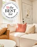 Sunny white living room with comfy sofa and throw pillows and blankets with Best list home essentials 2024 seal in upper left