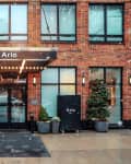 Entrance of Arlo Hotel with brick facade, large windows, potted plants, and snow falling.