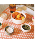 Hand reaching for cilantro on a patterned tablecloth with bowls of peppers, seeds, salt, and cream.