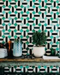 Geometric tiled wall with green and black pattern, wooden table, potted plant, glass vases, and stacked white plates.