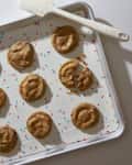 Cookies on a baking sheet with colorful sprinkles and a white spatula.