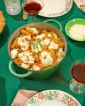 Green table with rigatoni in a pot, lemon pie, salad, baked pasta, red wine, and grated cheese.
