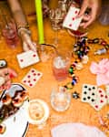 High Angle View Women Playing Card Game And Drinking Champagne At Table With Decorations And Candles At New Year's Eve Party