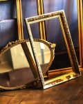 Gold ornate picture frames leaning against a dark wall on a wooden floor.