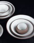 Stacked ceramic bowls and plates with brown rims on a dark surface.