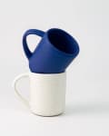 Two ceramic mugs stacked, one blue and one white with speckles, against a plain background.