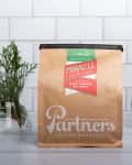 Bag of Partners Coffee Roasters Miracle blend with a green mug and a vase of greenery on a tiled background.