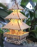 Wooden pagoda-shaped lamp illuminated among green potted plants.
