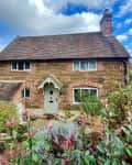 Charming stone cottage with a gabled roof, surrounded by lush garden plants.