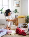 Woman sorting clothes for charity in a bright room with plants and books.