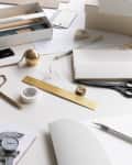 Office desk with drafting tools, gold ruler, scissors, pencils, eraser, and paper.