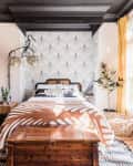 Bedroom with patterned wallpaper, wooden chest, orange throw, large windows, and yellow curtains.