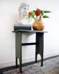 Bust sculpture and orange vase with flowers on a dark green console table.