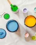 various bright colored paints in different sizes shot overhead. a can opener and a stirring stick in photo