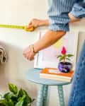 someone measuring a wall in their home before possibly hanging art, adding a piece of furniture, etc