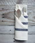 Fork and spoon wrapped in a striped cloth napkin on a rustic wooden table.