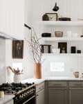 White kitchen with open shelves, gray cabinets, brass faucet, and decor items like cutting boards and vases.