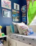 Child's bedroom with blue walls, colorful pillows, wall art, and green curtains.