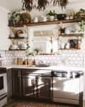 Cozy kitchen with hexagonal tile backsplash, open shelves with plants and dishes, dark cabinets, and a patterned rug.