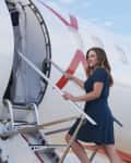 Woman in blue dress boarding a JSX Embraer jet via stairs on a sunny day.