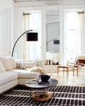 Living room with a cream sectional sofa, black floor lamp, round coffee table, and abstract wall art.