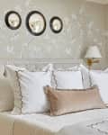 Elegant bedroom with floral wallpaper, beige headboard, white pillows, and gold wall lamps.