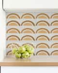Kitchen countertop with a wire basket of green apples and a backsplash of beige and white arch-patterned tiles.