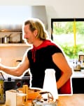 Man in a red cape holding a large bottle in a kitchen with chess pieces on the counter.