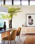 Modern living room with abstract art, wooden sideboard, mustard chairs, and a large potted fern.