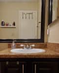 Bathroom with brown granite countertop, white sink, black framed mirror, and shelf with toiletries.