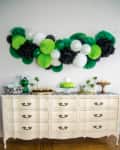 White dresser with green, black, and white paper decorations above, featuring a green cake and assorted desserts.