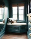 Cozy window nook with teal walls, striped ceiling, and patterned cushions on a cushioned bench.