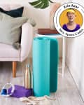 Living room with a pink sofa, patterned pillows, teal yoga mat, sneakers, water bottle, and exercise bands on the floor.