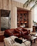 Spacious living room with leather sofas, wooden walls, large bookshelf, and tropical plants.