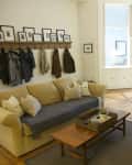Living room with beige sofa, wooden coffee table, framed photos, and coats on hooks, leading to a dining area.