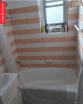 Bathroom with peach and white striped tiles, bathtub, towel, and toiletries on window ledge.