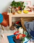 Cluttered room with a blue chair, laptop, drinks, plant, vinyl record, and scattered clothes and shoes on the floor.