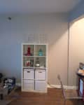 Living room with white cube shelf, "LOVE" letters on top, boxes, and a clear chair by a desk.